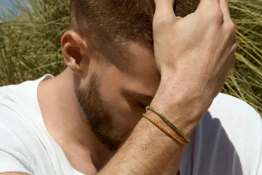 Gros plan d’un homme tenant sa tête, portant deux bracelets fins en or jaune et vert de la collection Bracelets Kern.